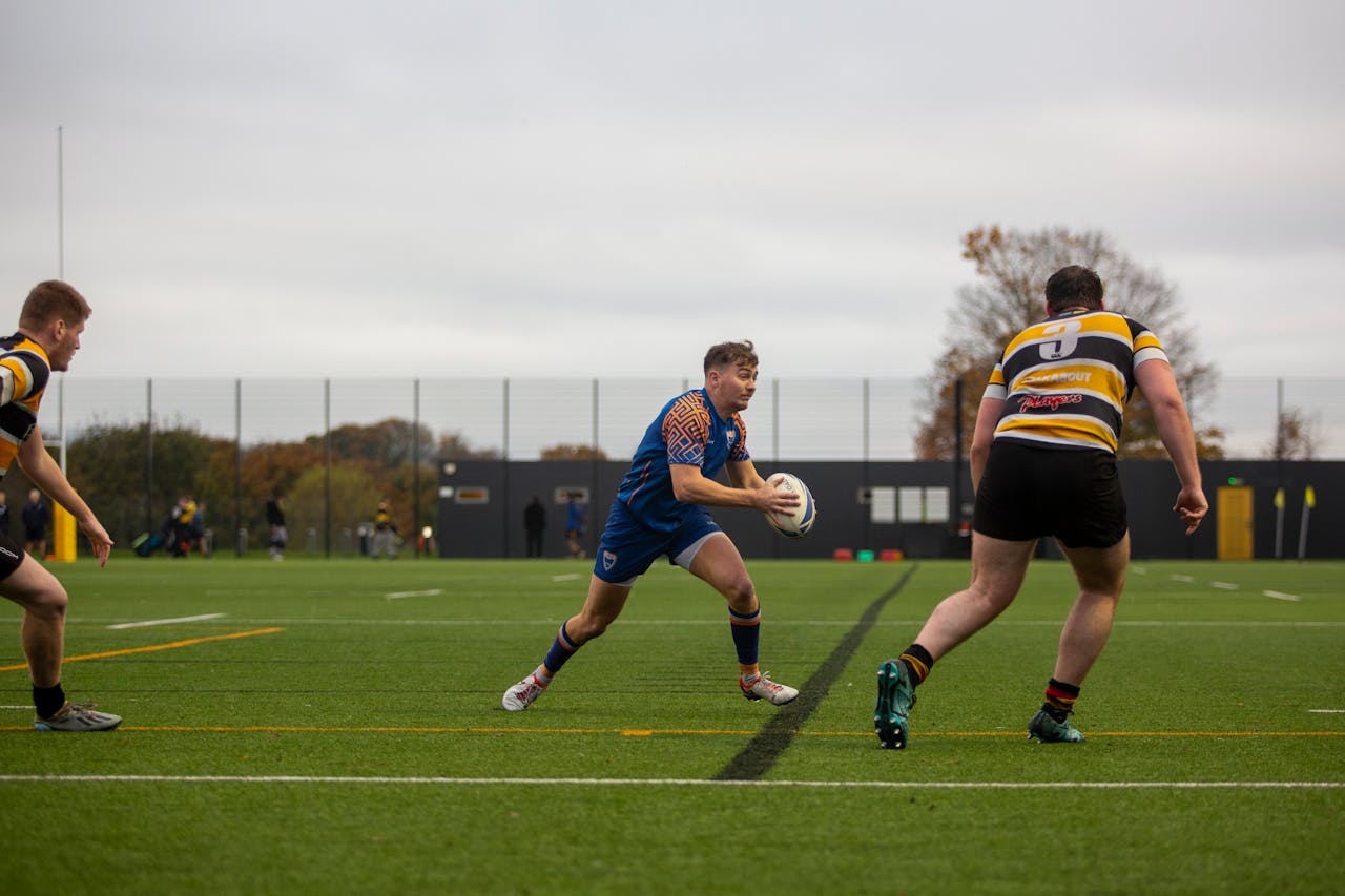 University rugby players in action during an outdoor rugby match on a sports field.