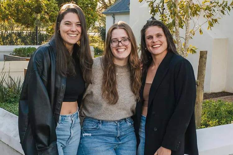 Olympic rugby star Ilona Maher smiling warmly outdoors alongside her sisters, Olivia and Adrianna Maher, showcasing her close-knit family background.