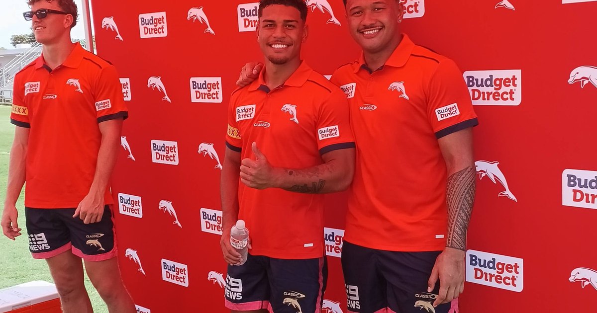 Three Dolphins players in red training shirts posing in front of a sponsor wall