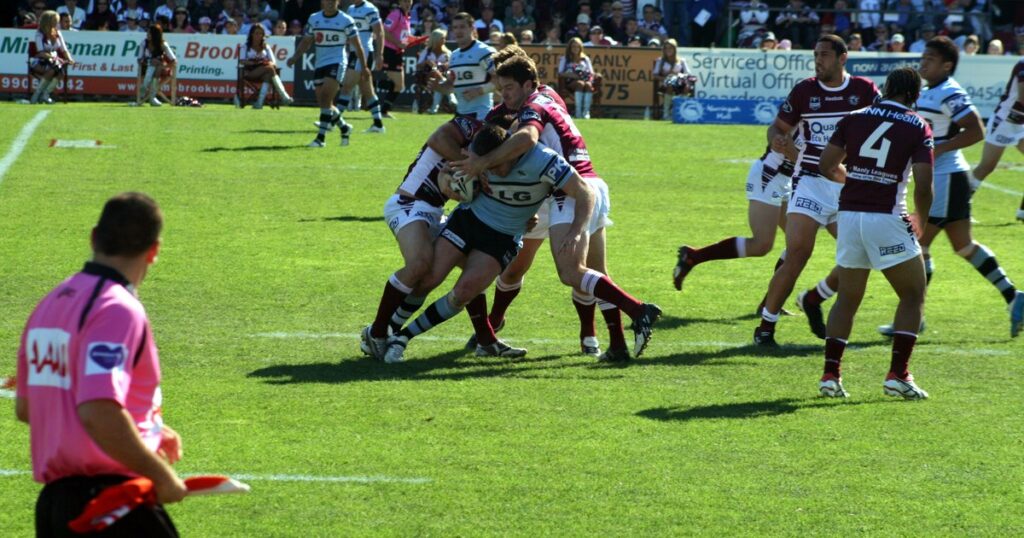 Two defenders completing a tackle in an NRL match with a touch judge in the foreground