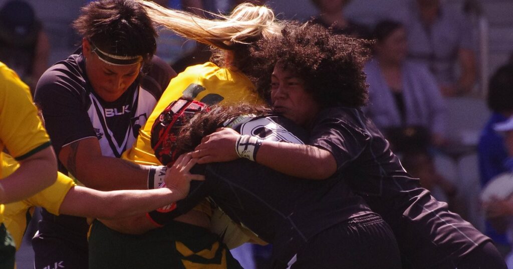 New Zealand women's rugby league players in black making a tackle on an Australian player