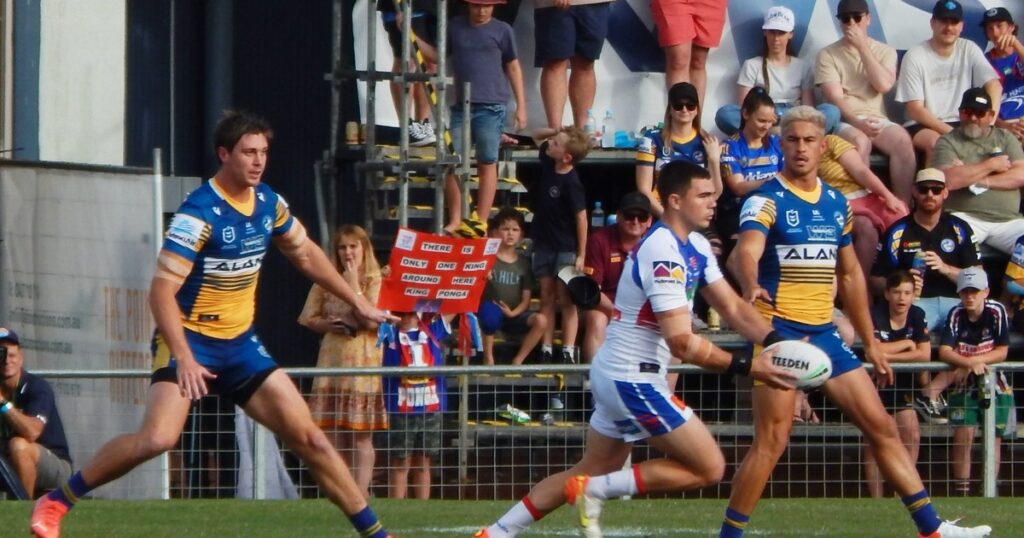 A Newcastle Knights player in play with a crowd sign reading King Ponga behind