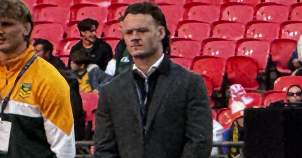 Ethan Strange in a dark suit standing pitchside at Wembley with Australian staff