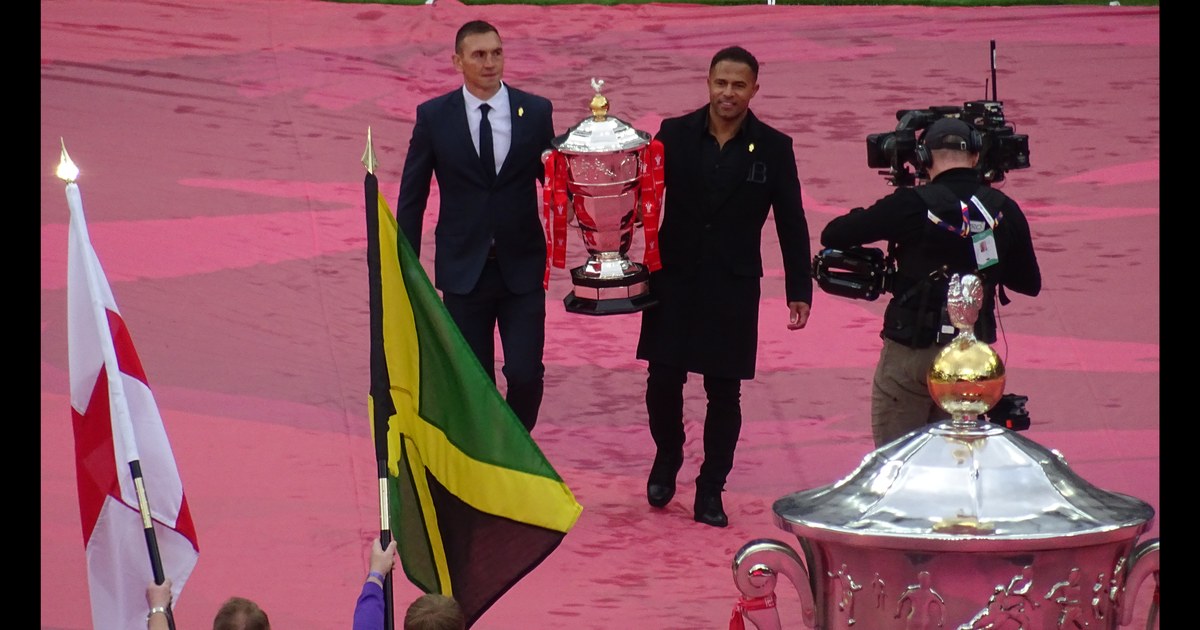 Two former players carrying the Rugby League World Cup trophy onto the pitch