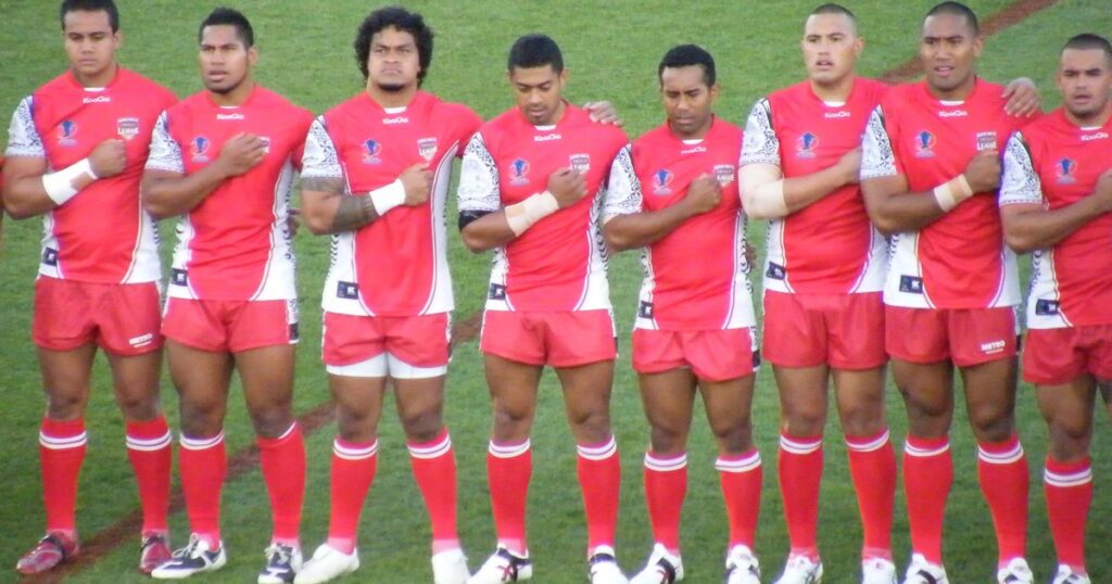 Tonga rugby league players in red jerseys lined up arm in arm for the anthem
