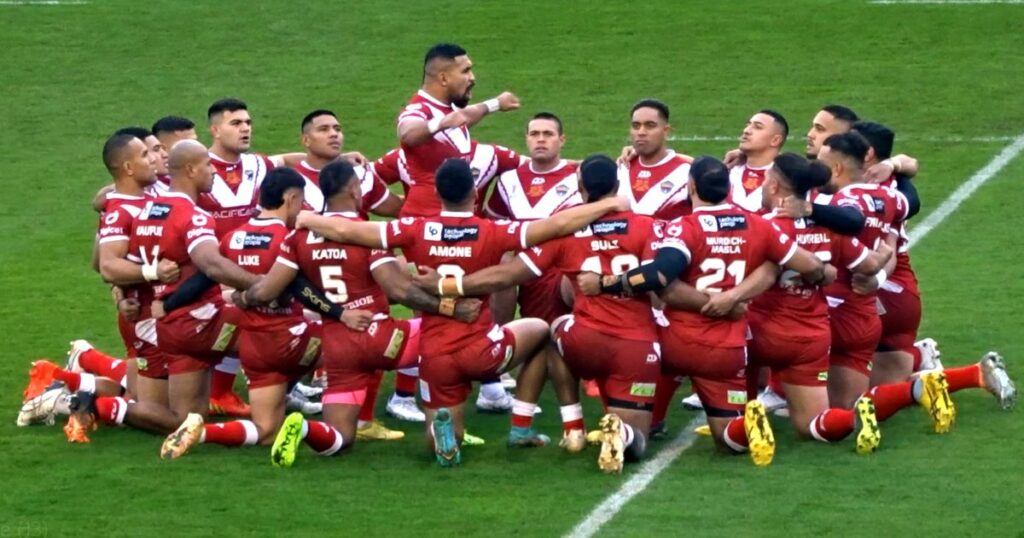 Tonga players in red kneeling and crouching together on the pitch during the Sipi Tau