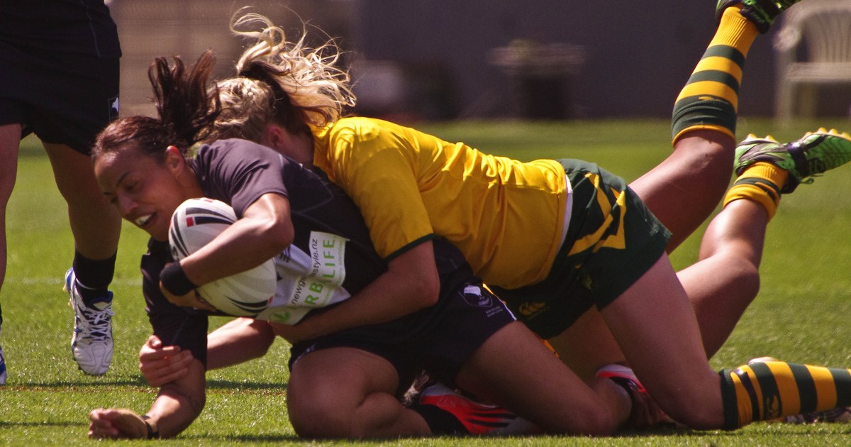 A women's rugby league player being tackled as she scores